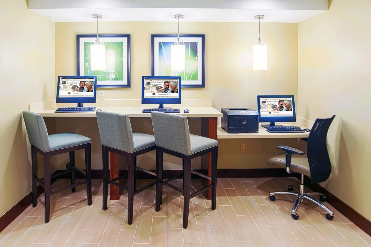 A well-lit business center featuring several computers set up on a counter, complemented by modern bar stools and contemporary light fixtures. Framed artwork adds a touch of sophistication, while the layout invites guests to work, browse the internet, or print documents in a productive environment.