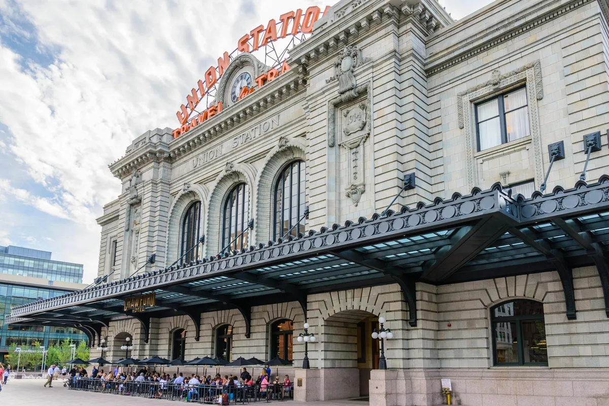 This image prominently features the grand facade of Union Station with its iconic sign, bustling outdoor seating area, and vibrant patrons enjoying the energetic atmosphere. Architectural details add a sense of local character and sophistication.