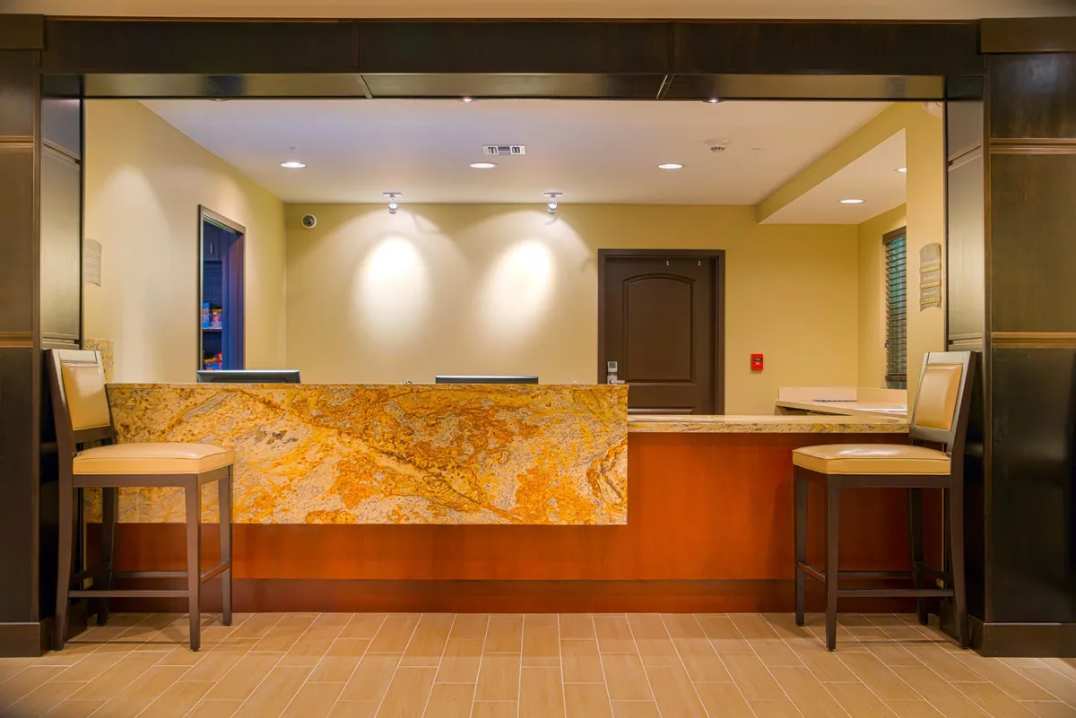 A welcoming reception area with a comfortable seating arrangement and inviting lighting, where guests are being checked in and can relax while waiting. The atmosphere is friendly, with amenities like refreshments available.