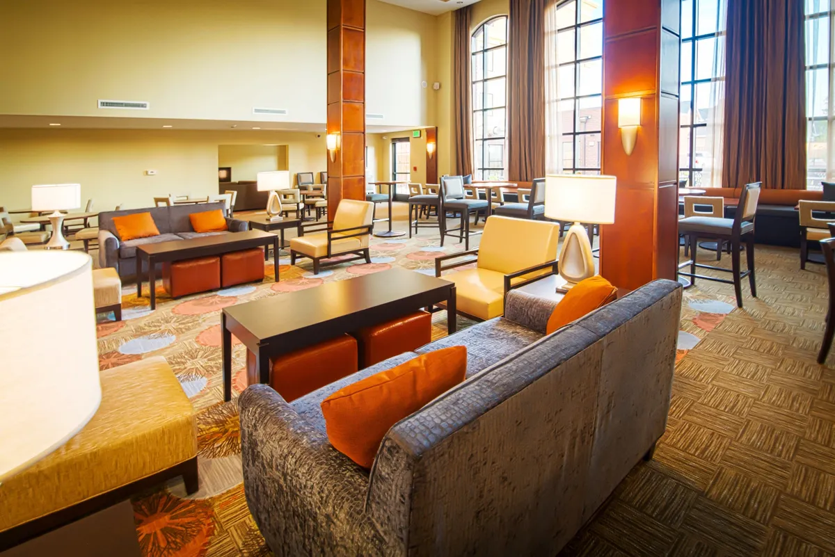 A spacious, airy living area filled with natural light from large windows. Comfortable seating is arranged for socializing or relaxation, and modern decorative light fixtures add a warm, inviting feel.