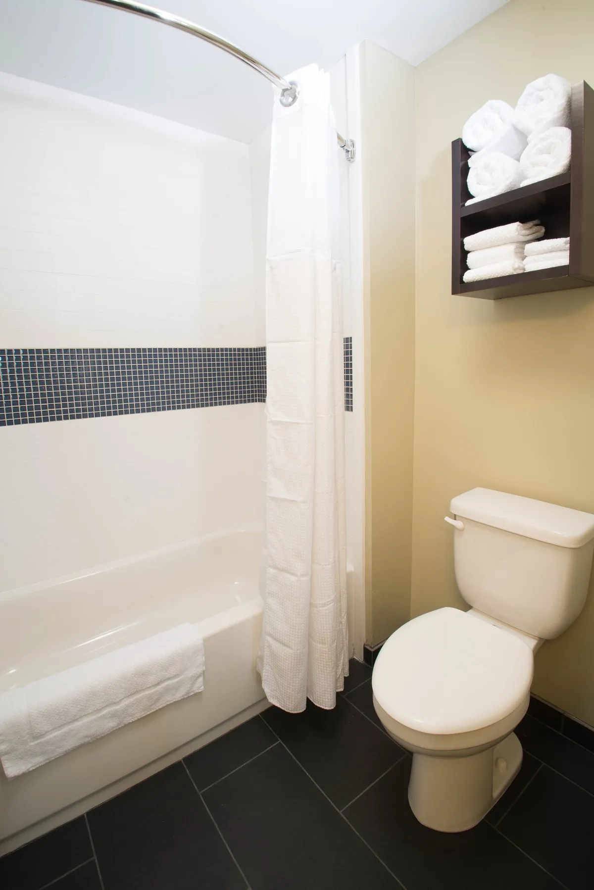 A modern, well-equipped bathroom featuring a bathtub, toilet, towel rack, and shower curtain. Fresh towels are neatly arranged, and the clean, inviting decor promotes relaxation and convenience.