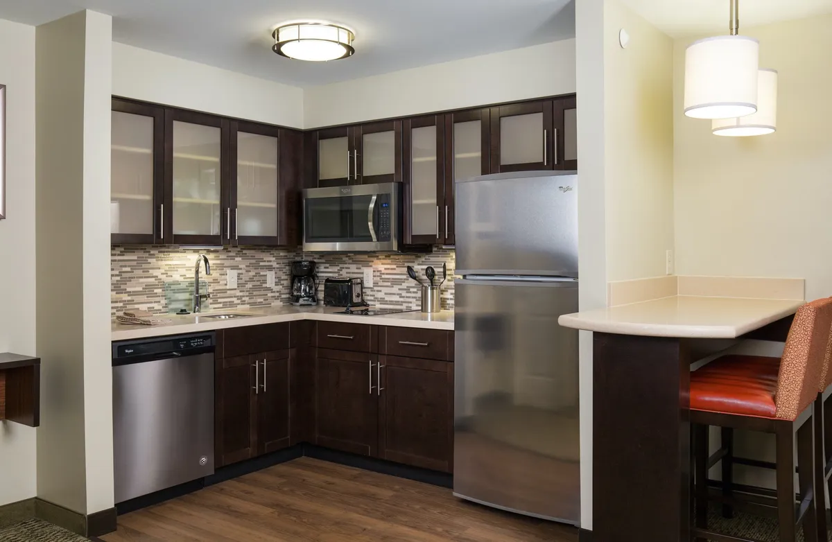 A bright, modern kitchen featuring sleek cabinetry, stainless steel appliances including a stove and refrigerator, and a spacious bar seating area. The countertop is clear, inviting guests to cook, dine, or socialize. The open layout is designed for effortless meal preparation and comfortable gatherings.
