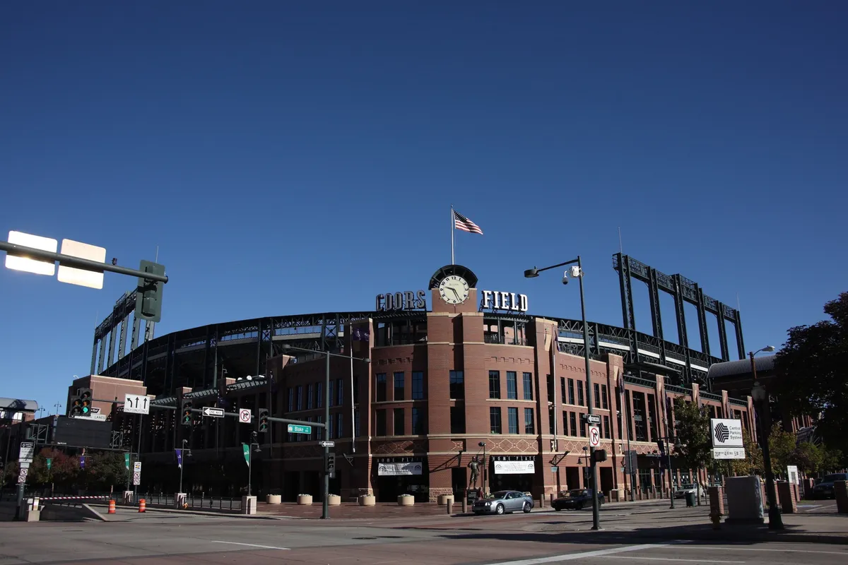 This image captures the exterior of Coors Field, with the iconic stadium, American flag, and surrounding busy streets. People can be seen gathering for a game, contributing to an exciting city atmosphere.
